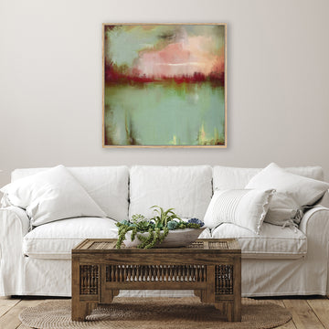 Abstract canvas art print of a sage green lake and crimson sunset, displayed above a white linen couch in a country-style living room.