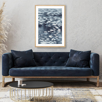 Inky black and white framed art print of a moonlit waterlily pond above a midnight-blue velvet couch.