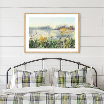 Framed art print of a watercolour landscape artwork in green and gold displayed in a country-style interior.