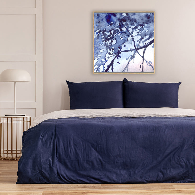 Art print of foliage-laden branches in indigo-blue, silhouetted against a moonlit sky, in a bedroom with navy bed covers.