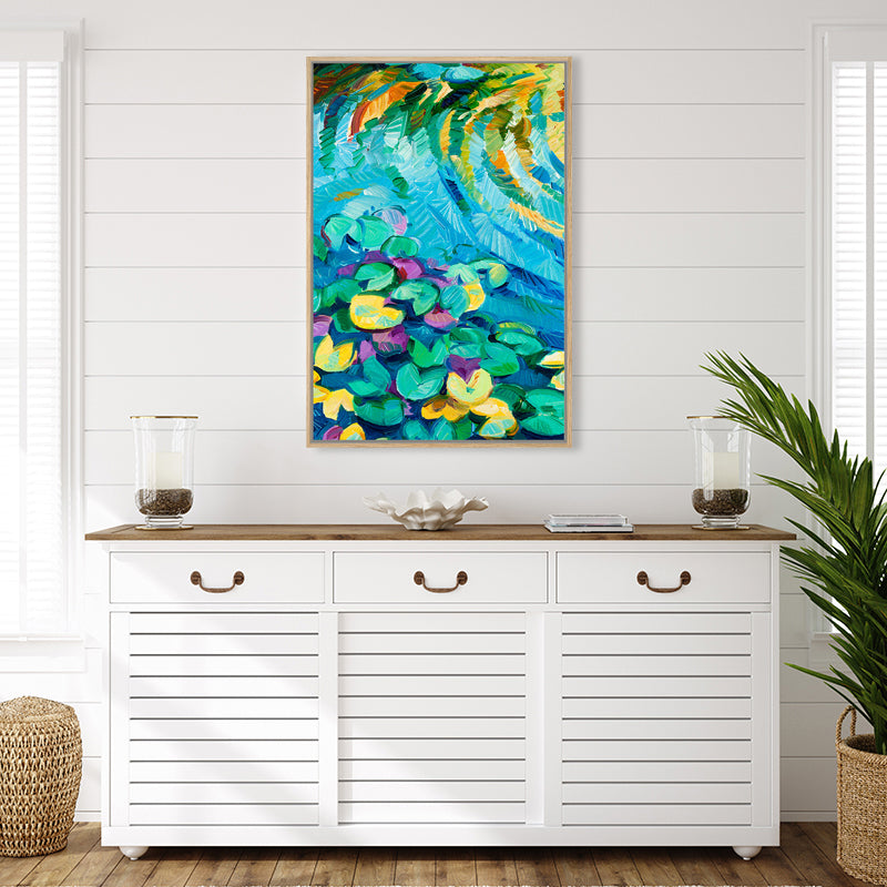 Framed canvas art print of an aqua blue pond with green and yellow lily pads, in a white tropical-style interior.