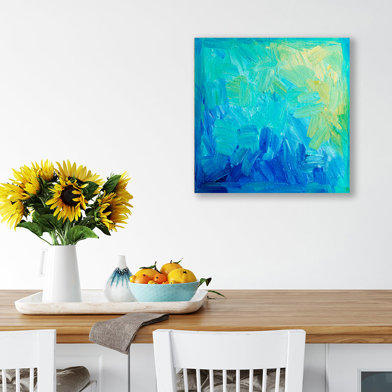 Abstract artwork in aqua, sapphire, and yellow hanging above a dining table with a vase of sunflowers.