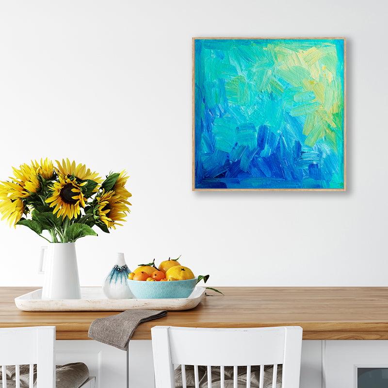 Abstract artwork in aqua, sapphire, and yellow hanging above a dining table with a vase of sunflowers.