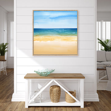 Framed canvas art print of an aquamarine sea set between coral sand and azure blue sky in a coastal-style interior.