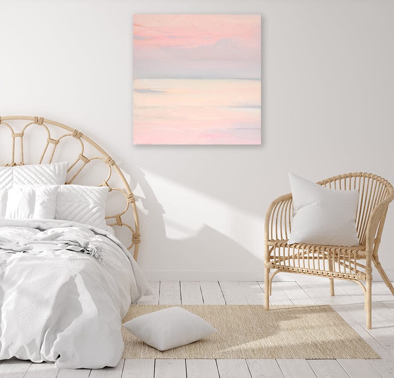 Pale pink sky and sea canvas art print in a light-filled white bedroom with cane furniture. 