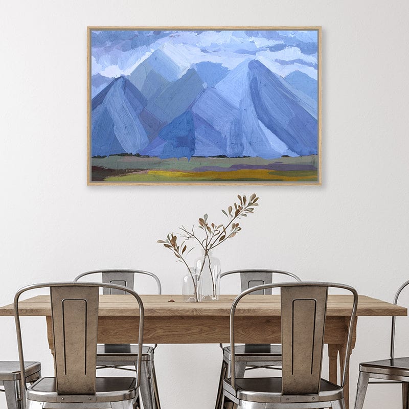 Abstract expressionist oak framed canvas art print of denim blue mountains beneath a cloudy sky in a modern farmhouse style dining room.