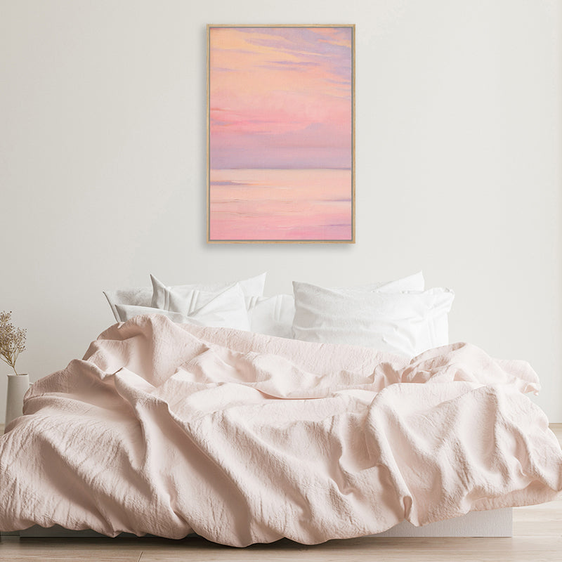 Canvas wall art print of a lavender pink sky above a calm sea in a minimalist white and pastel pink bedroom.