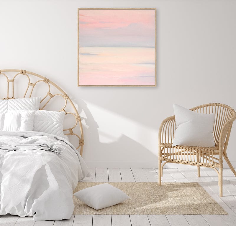 Pale pink sky and sea framed canvas wall art print in a light-filled bedroom with cane furniture.