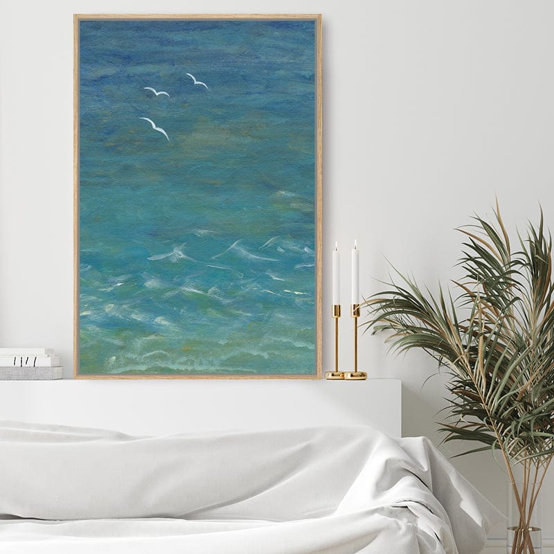 Framed art print of the sea from above with seagulls and white breakers standing out against turquoise water in a romantic white bedroom.  