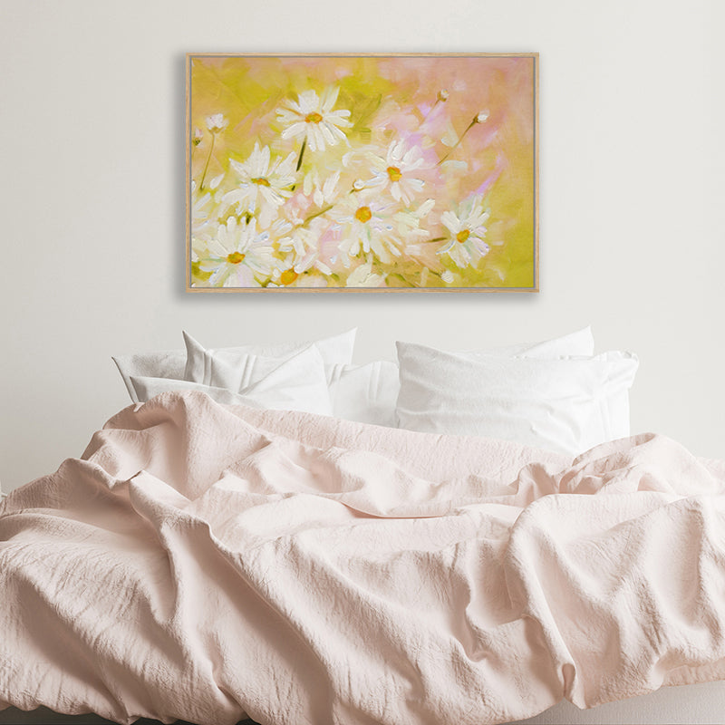 Framed canvas art print of white daisies on a mustard yellow and pink background in a soft minimalist bedroom.